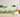 Hand-painted style grass wall decals in various shades of green, arranged against a soft blush pink background. The image features layered blades of grass and a few round leafy shapes, designed to mimic natural foliage with a watercolor texture.